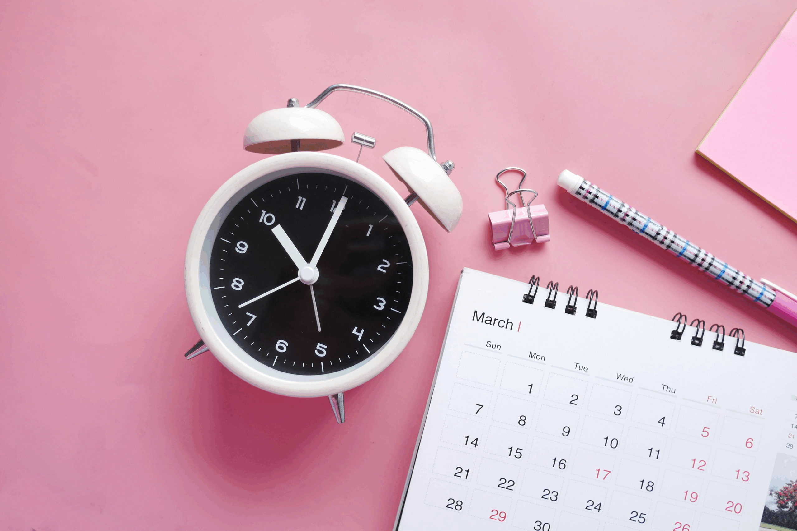 a clock with calendar on pink backdrop