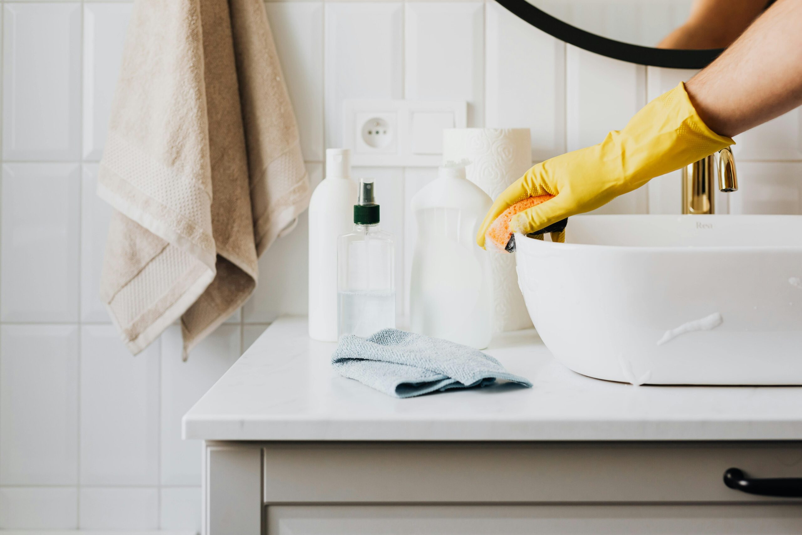 A woman wearing yellow gloves wiping the sides of a bathroom sink.