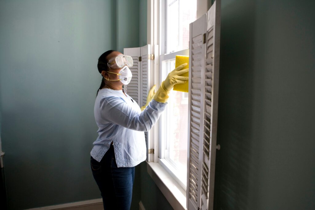 A cleaning lady wearing yellow gloves scrubbing the window.